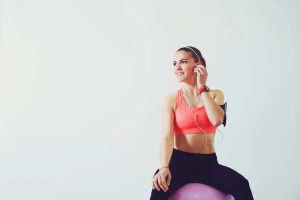 Junge sportliche Frau, die mit Smartphone im Studio auf Ball sitzt. Fitness, Lifestyle, Technologie und People-Konzept. Kopierraum. — Stockfoto