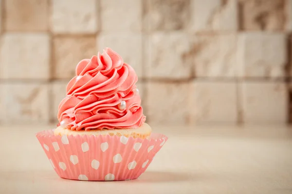 Roze lekkere cupcake op tafel op bakstenen muur achtergrond. — Stockfoto