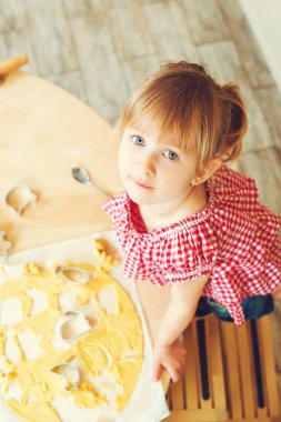 Sevimli küçük kızını kurabiye hamuru farklı şekillerde kesiyor. Kızın annesi fırında kurabiye bir mutfakta yardımcı olur..