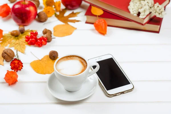 Fundo de outono, xícara de cappuccino perto do telefone móvel na mesa de madeira . — Fotografia de Stock