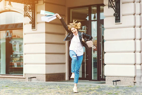 Mulher atraente alegre pulando com sacos de papel depois de boas compras . — Fotografia de Stock