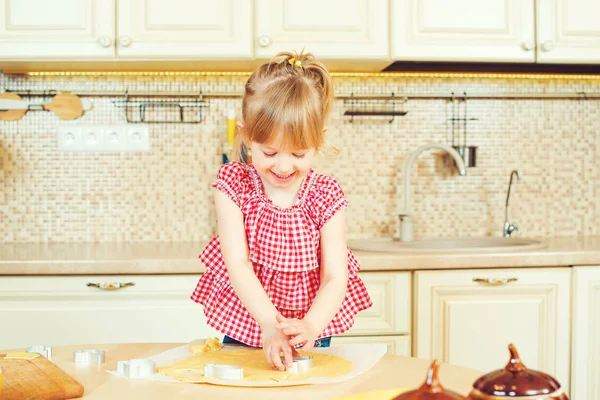 Carino bambina aiutando sua madre cuocere i biscotti in una cucina . — Foto Stock