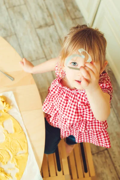 Sevimli küçük kızını kurabiye hamuru farklı şekillerde kesiyor. Kızın annesi fırında kurabiye bir mutfakta yardımcı olur..