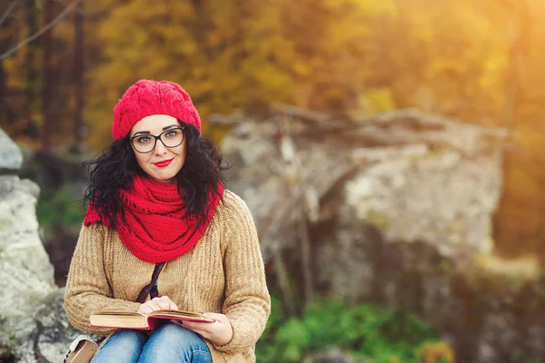 Attractive young woman reads book in a park and enjoys sunny autumn day. — Stock Photo, Image