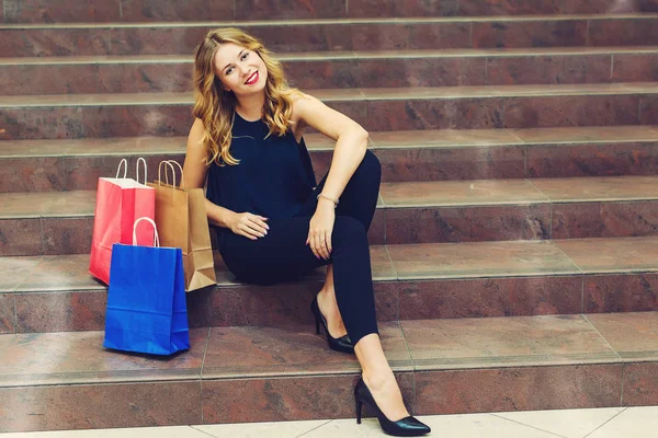 Красивая молодая женщина сидит на лестнице во время шоппинга с сумками в магазине . — стоковое фото
