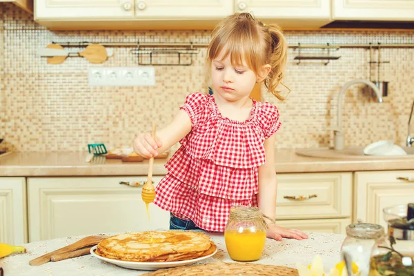 Sevimli küçük kız hazırlamak krep ve gözleme yığınının üzerine dökerek bal.