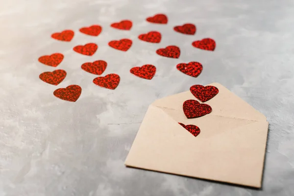 Kuvert från craft papper med röda hjärtan heap sprids på grå bakgrund. — Stockfoto