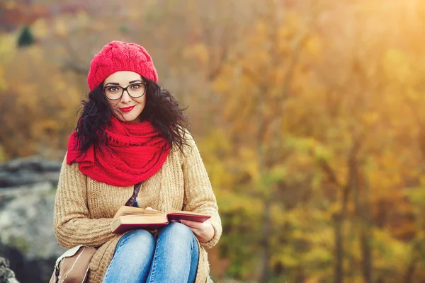 Atrakcyjna młoda kobieta czyta książkę w parku i oferuje słoneczny jesienny dzień. — Zdjęcie stockowe