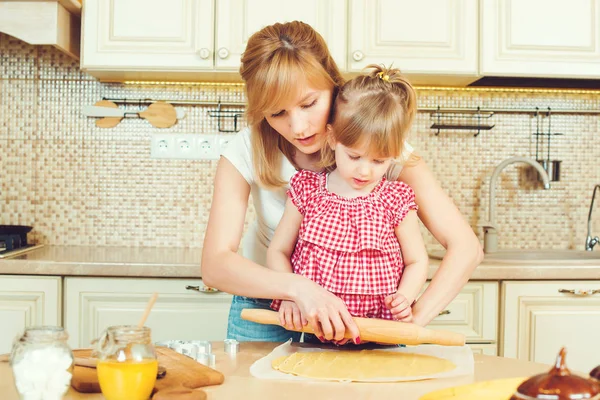 Giovane madre e piccola figlia carina cuocere i biscotti e divertirsi in cucina . — Foto Stock