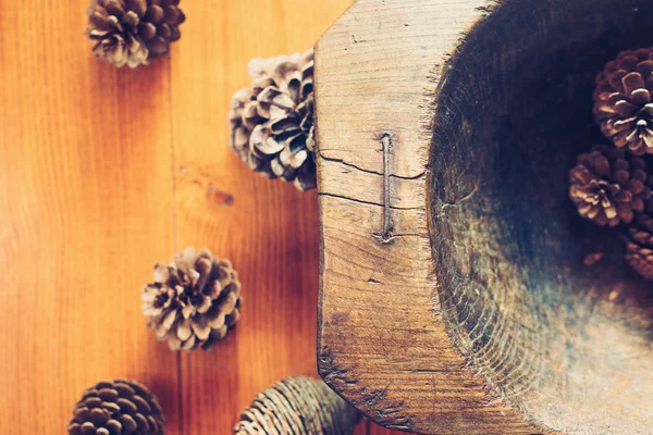 Many pine cones in old wooden bowl on table.