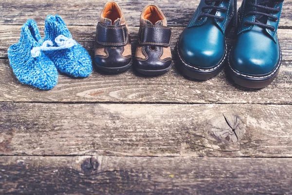 Zapatos para niños diferentes sobre fondo de madera oscura. Zapatos de punto de bebé y botas de cuero para niños para clima frío . — Foto de Stock