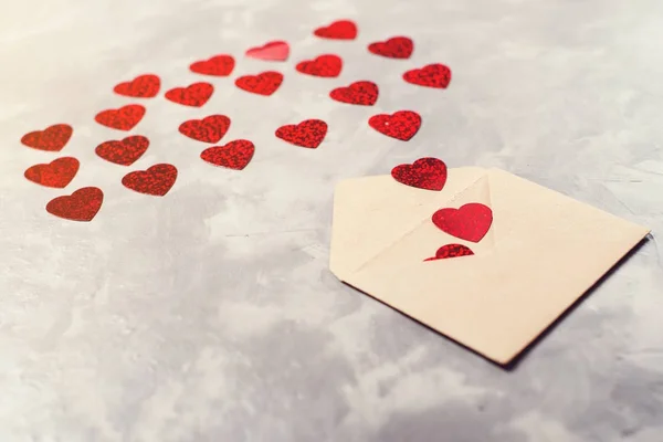 Конверт з ремісничого паперу з червоними сердечками, розкиданий на сірому фоні . — стокове фото