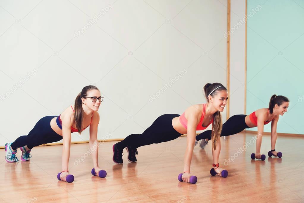 Group of young women in sportswear with dumbbells exercising at the gym.