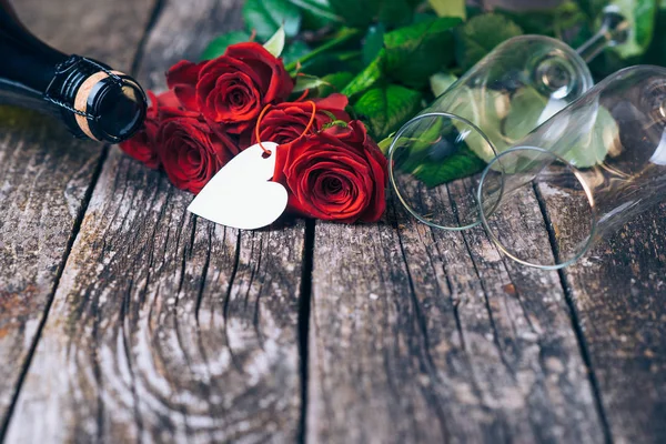 Bouquet of red roses, two glasses, bottle of wine, gift box with tag on vintage wooden board. Valentines day. — Stock Photo, Image