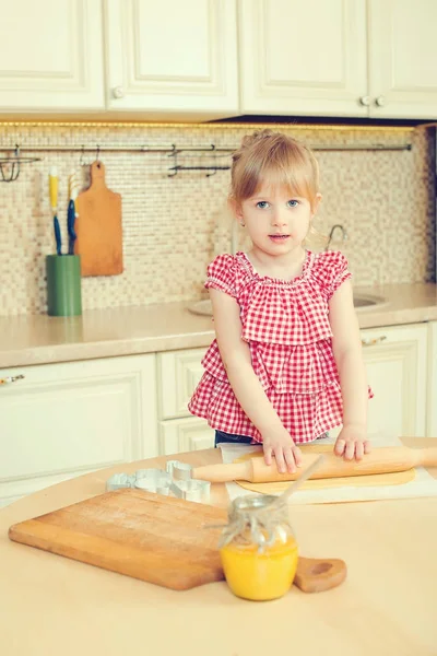 Schattig klein meisje helpt haar moeder bak koekjes in een keuken. — Stockfoto
