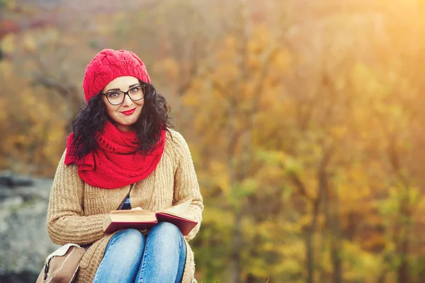 Atrakcyjna młoda kobieta czyta książkę w parku i oferuje słoneczny jesienny dzień. — Zdjęcie stockowe
