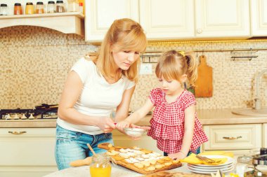 Genç anne ve sevimli küçük kızı çerezleri ve mutfakta eğlenerek fırında.