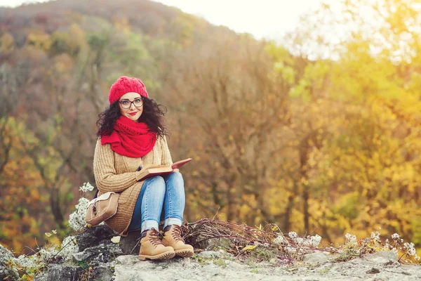 Aantrekkelijke jonge vrouw leest boek in een park en geniet van de zonnige herfstdag. — Stockfoto