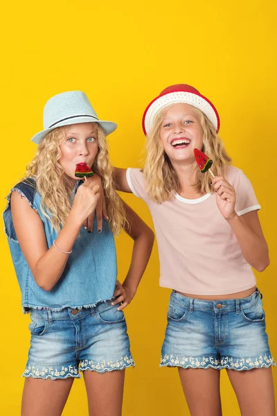 Chicas gemelas sosteniendo piruleta y divertirse juntos sobre fondo amarillo . — Foto de Stock