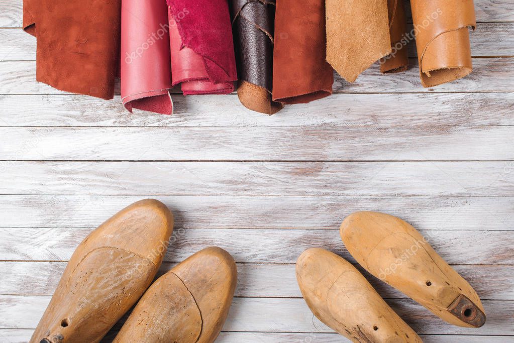 Set of cobbler tools and a lot of brightly colored leather in rolls on the wooden background. Space for text.