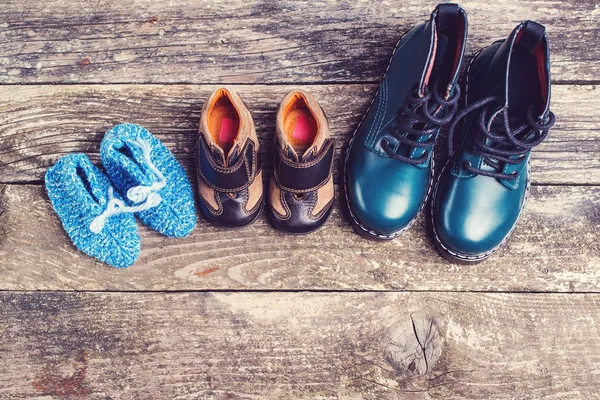 Zapatos para niños diferentes sobre fondo de madera oscura. Zapatos de punto de bebé y botas de cuero para niños para clima frío . — Foto de Stock