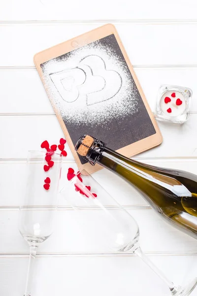 Two glasses, champagne and chalkboard with decorative hearts on white wooden background. Valentines day card. — Stock Photo, Image