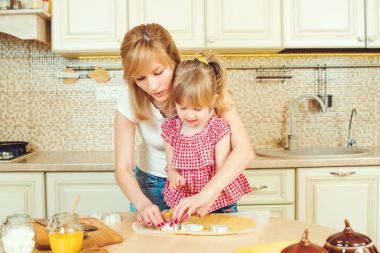 Sevimli küçük kız ve annesi çerez kesici, bir mutfakta kırpılmış kullanarak çerezleri hazırlanıyor.