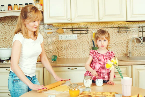 Giovane madre e piccola figlia carina cuocere i biscotti e divertirsi in cucina . — Foto Stock