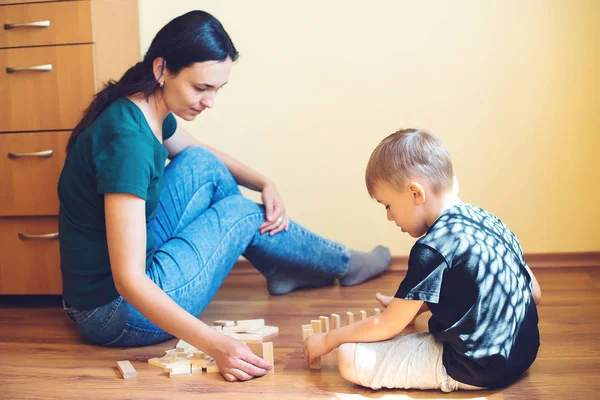 Young mother and son playing with wooden blocks indoor. Happy family spends time together at home.