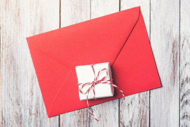 Kırmızı zarf ve ahşap arka plan üzerinde küçük bir hediye. Üstten Görünüm, kopya alanı.