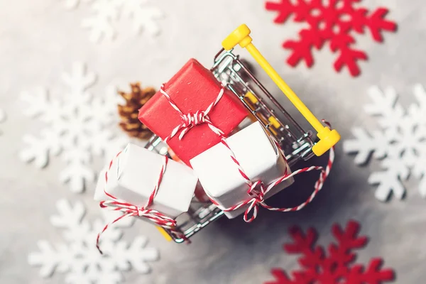 Karácsonyi ajándék dobozok egy bevásárlókocsi-ban felső szürke háttér, dekoratív snowflackes körül, felülnézet. Karácsonyi értékesítési koncepció. — Stock Fotó