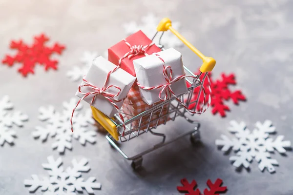 Kerstcadeau selectievakjes in een winkelwagentje over grijze achtergrond met decoratieve snowflackes rond, selectieve aandacht. Kerstmis verkoop concept. — Stockfoto