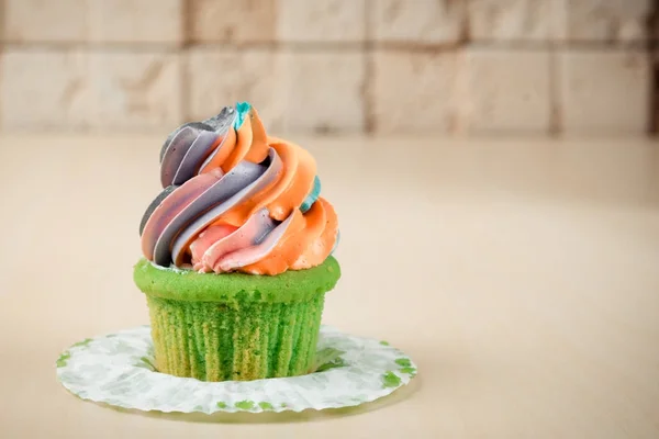 Kleurrijke regenboog cupcake op tafel op bakstenen muur achtergrond. — Stockfoto