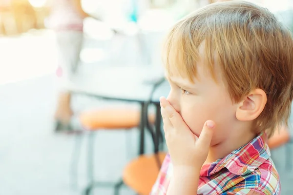 Pieni poika peittää suunsa käsillään, ulkona — kuvapankkivalokuva