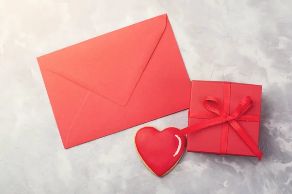 Valentinskarte mit rotem Umschlag, Geschenkschachtel und Herz-Lebkuchen auf grau strukturiertem Hintergrund. — Stockfoto