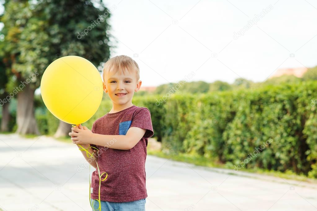 Little funny boy play with yellow balloon outdoor.