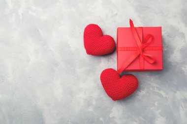 Kırmızı hediye kutusu gri dokulu arka plan üzerinde yatıyordu yakınındaki iki örgü kalp ile.