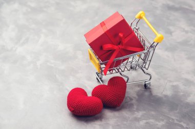 Kırmızı hediye kutusu gri texyured arka plan üzerinde iki örgü kalp ile alışveriş arabası.