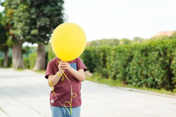 Kleiner lustiger Junge spielt mit gelbem Ballon draußen. — Stockfoto