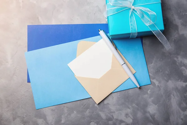 Moderna caja de regalo azul con sobres para tarjeta de felicitación sobre fondo de hormigón. Tarjeta vacía con pluma blanca . — Foto de Stock