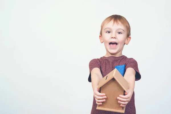 Niedlichen kleinen Jungen halten eine kleine Hausbank. Konzepte, die Geld für Haus und Zukunft sparen. — Stockfoto