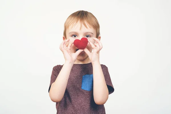Schattige gelukkige jongen spelen met rood gebreide hart, geïsoleerd op witte achtergrond. — Stockfoto