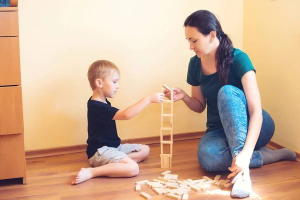 Young mother and her son playing with wooden blocks indoor. Happy family spends time together at home.