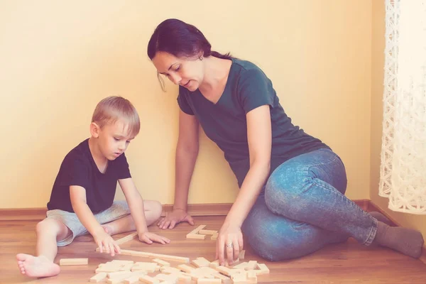 Young mother and her son playing with wooden blocks indoor. Happy family spends time together at home.