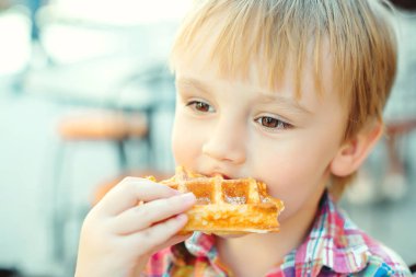 Sevimli küçük çocuk yaz terasında leziz Belçika waffle yiyor.