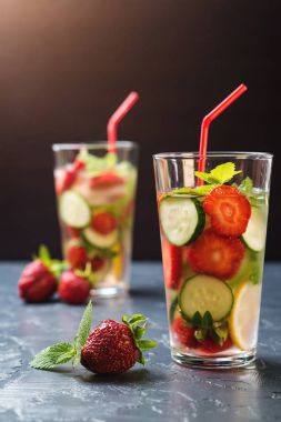 Soğuk ve ferahlatıcı Detoks su çilek ve siyah arka plan üzerine cam içinde salatalık ile infüzyon.