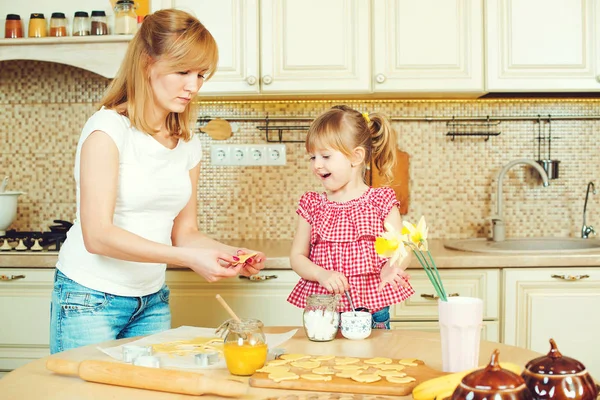 Giovane madre e piccola figlia carina cuocere i biscotti e divertirsi in cucina . — Foto Stock