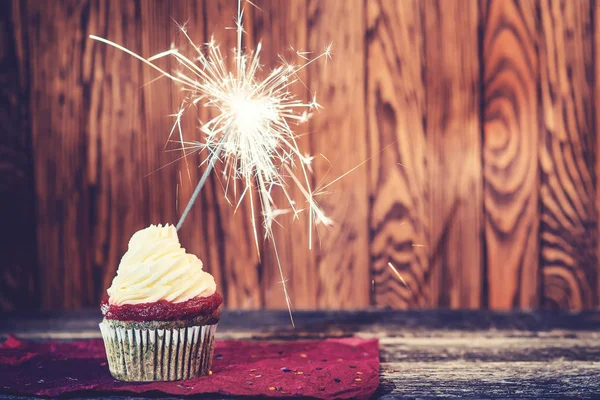 Cupcake with cream cheese, with sparkler on dark wooden background. — Stock Photo, Image