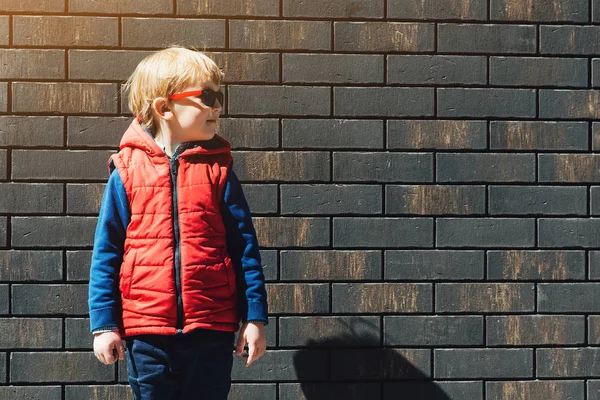 Schattige kleine jongen in trendy zonnebril opzij buitenshuis op zoek. — Stockfoto