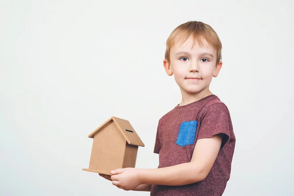 Schattige kleine jongen houdt een klein huis bank. Concepten opslaan van geld voor het huis en de toekomst. — Stockfoto